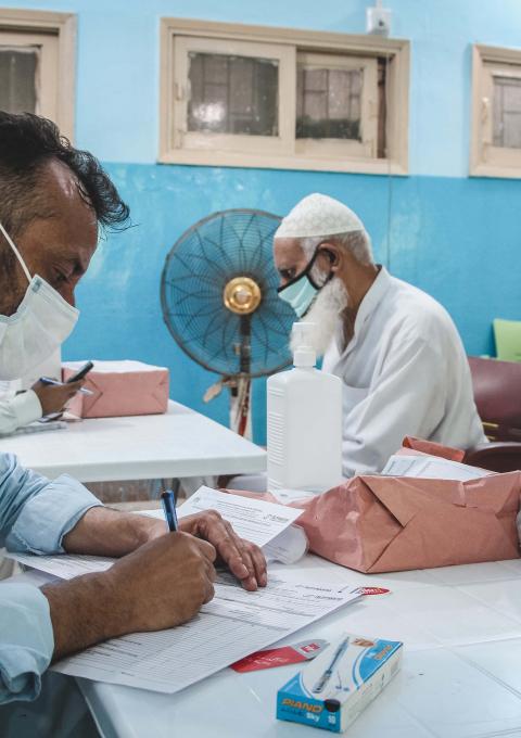 An MSF doctor taking the medical history of someone coming for their COVID-19 vaccination. They check if he has any symptoms of COVID, or is currently taking any medication. 
