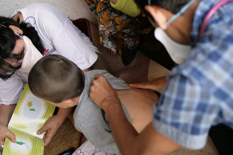  In Dushanbe, Tajikistan, MSF doctor Kartik Chandria examines a young boy suffering from multi-drug resistant tuberculosis (MDRTB) as a mental health counselor distracts him with a TB health education book.