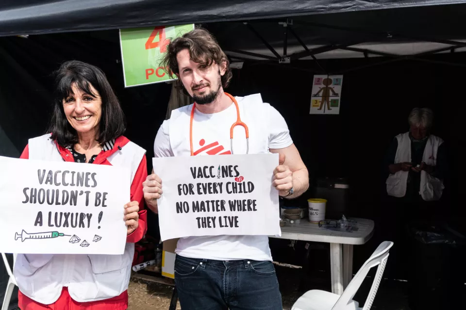 MSF medical staff, Corinne Peters and Stefanos Tsallas holding signs advocating for broader use of the pneumonia vaccine at a lower price
