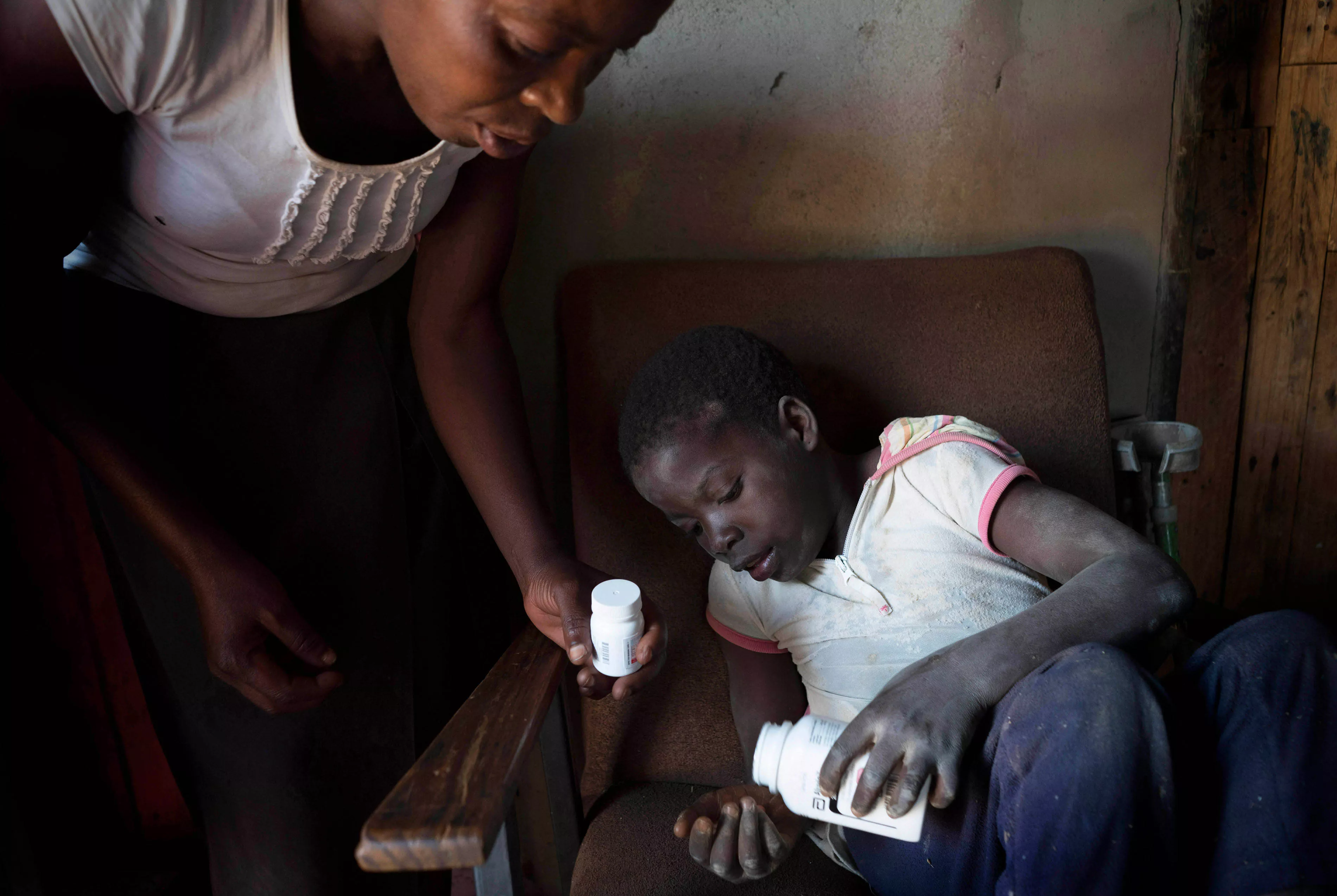 Ten year old Tanya, who is HIV positive and unable to walk, takes her medication with the help of her neighbor Florence who she calls ‘Mama’. Her mother died in 2010. Florence, Tanya and her mother we all part of the first group of patients to join MSF and the Ministry of Health and Childcare’s Epworth HIV program a decade ago, 28 October 2016. 