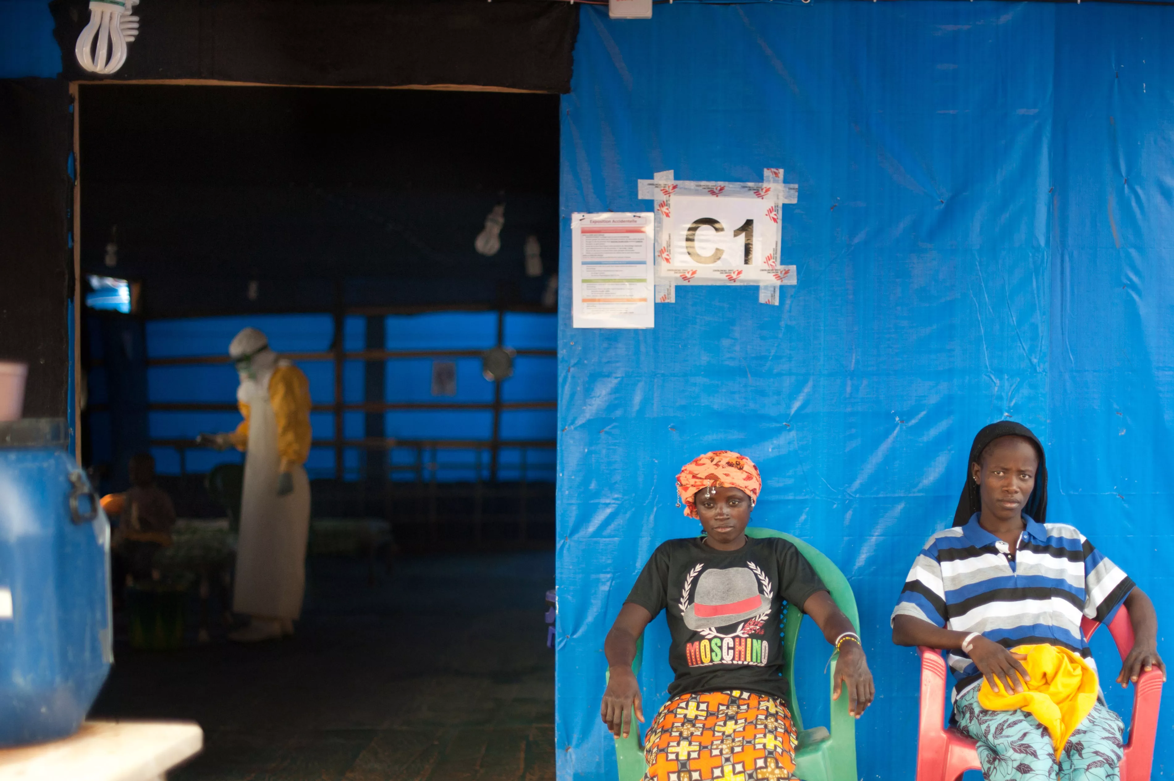 In the MSF Ebola Treatment Center in Guéckédou, Finda (left), and Kadia (right), two Ebola patients participating in the favipiravir trial, relax outside their ward. Inside, MSF staff care for a five year old boy whose mother died from Ebola the previous day.