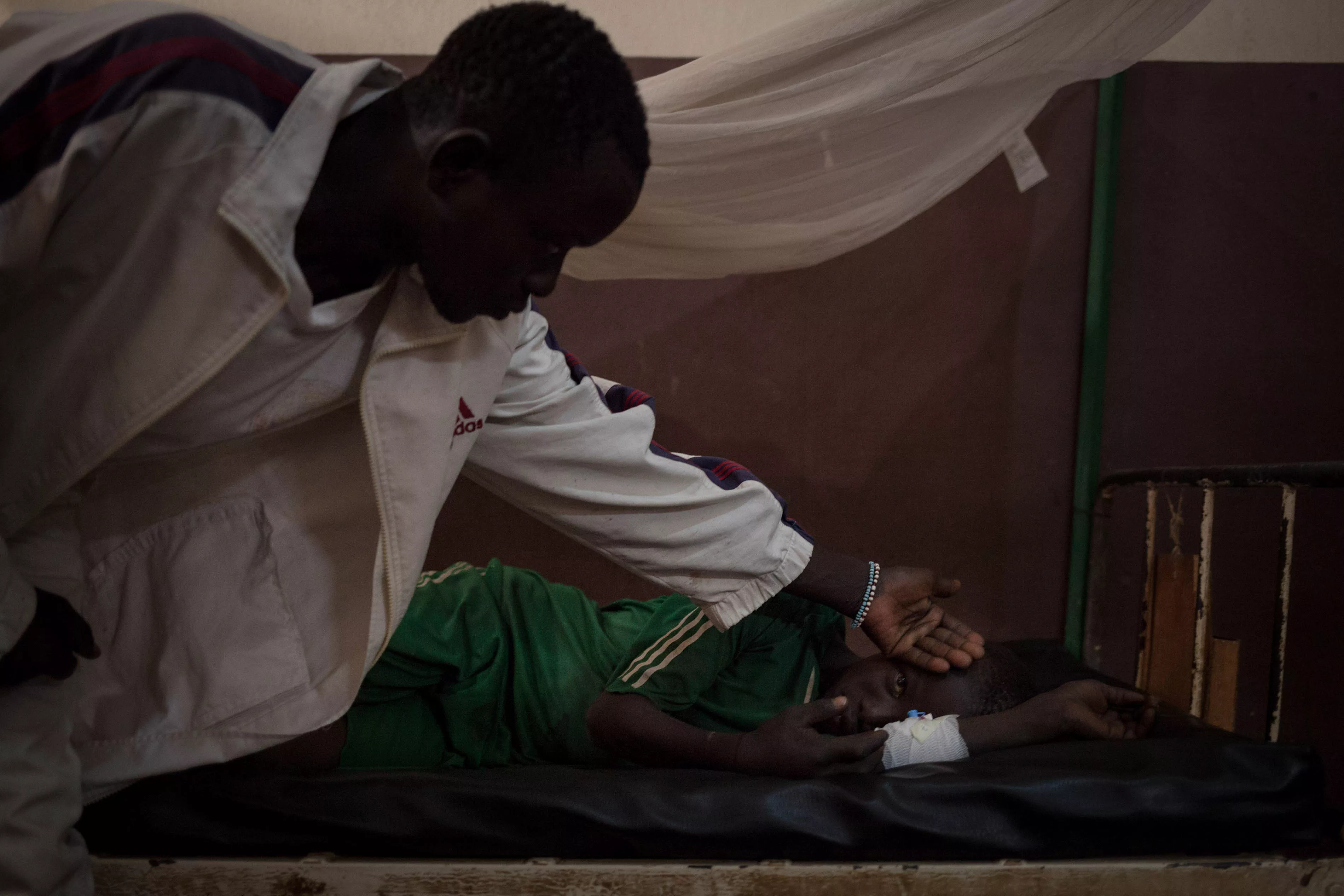 Nicsonne Dadjam, 13, is treated at Paoua Hospital, northwestern Central African Republic, supported by MSF. He was bitten by a snake while working in the fields in his village, 2 hours by motorbike from Paoua. His older brother is checking his temperature, 2018.