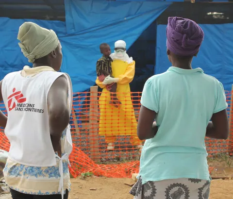 Helena gets a chance to talk to her son Moses who is an Ebola confirmed patient. A MSF health promoter supports this difficult moment for the young mother as she is too overwhelmed with what to say. The health promoter advises her to say positive things such as "I am waiting here outside for you“ or "I am thinking of you non Stop“.