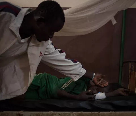 Nicsonne Dadjam, 13, is treated at Paoua Hospital, northwestern Central African Republic, supported by MSF. He was bitten by a snake while working in the fields in his village, 2 hours by motorbike from Paoua. His older brother is checking his temperature, 2018.