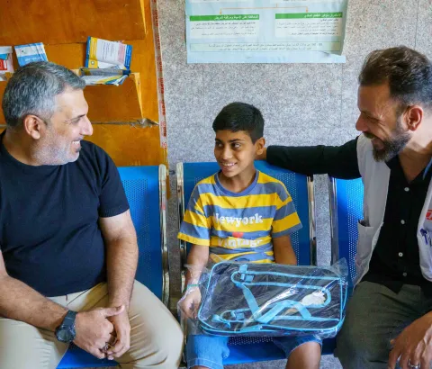 Abu Al-Fadl, a young boy diagnosed early with tuberculosis, sits with his father and an MSF health promoter at Mustafa Al-Adhari Health Center in Sadr City. After completing his treatment, he has recovered and will soon return to school..
